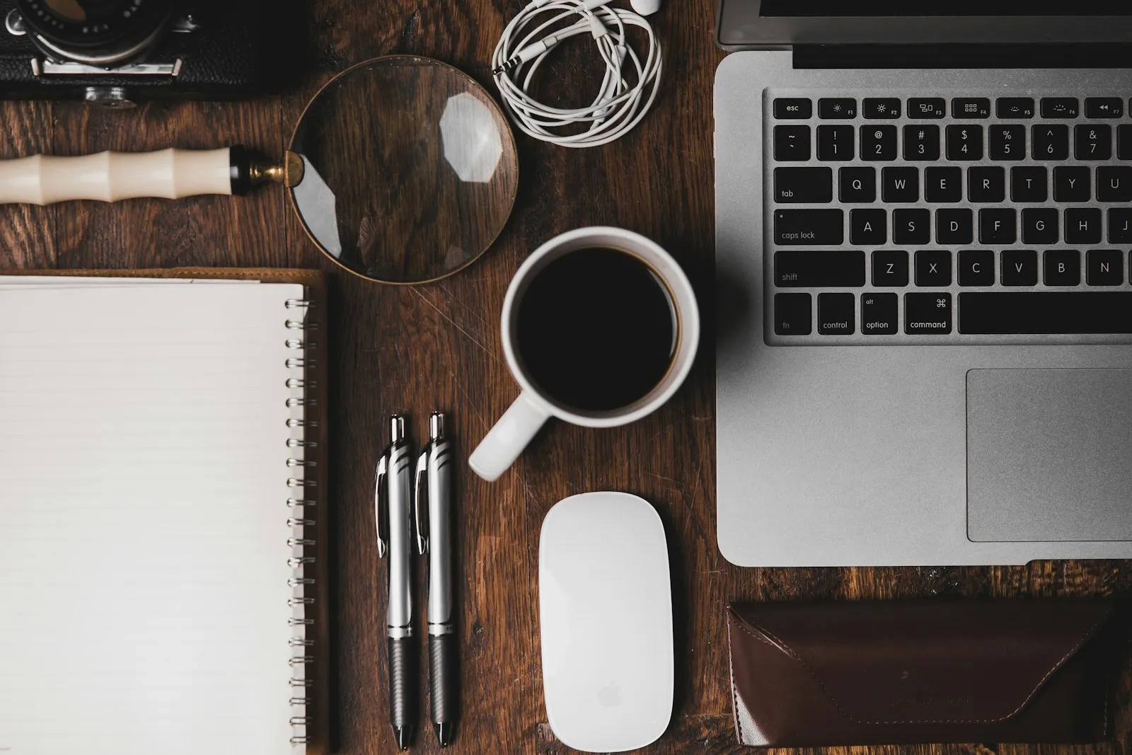 A creative's desk from above: laptop, open notebook, camera, and coffee.